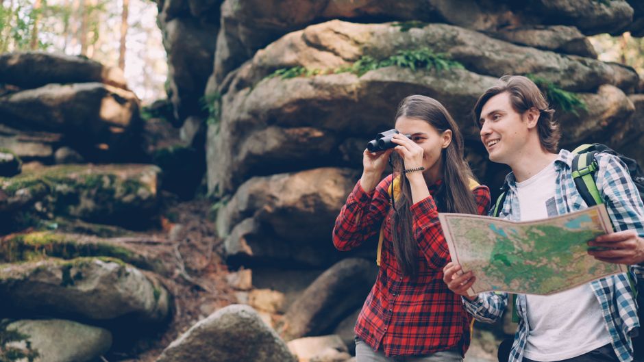 Two young adults exploring nature with map and binoculars among rocks.
