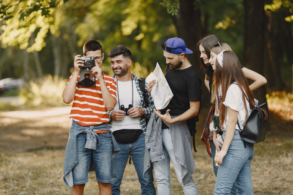 A group of young adults hiking and exploring with a map and camera in a forest setting.